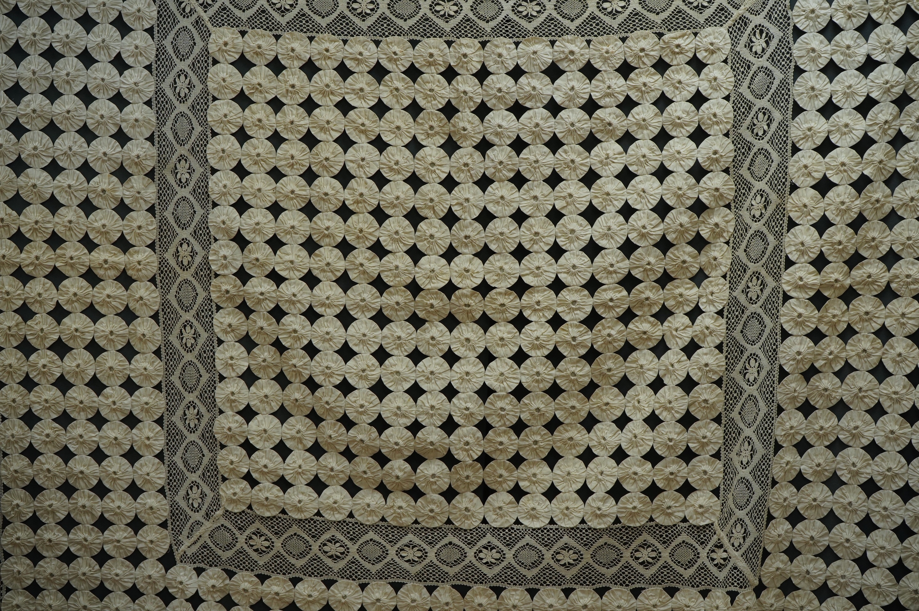 A late 19th early 20th century ‘YoYo’ puffy cream silk and cream bobbin lace quilt/bedcover, made with circles of silk, drawn together as a decorative gathered to top, then stitched together in panels and between wide bo